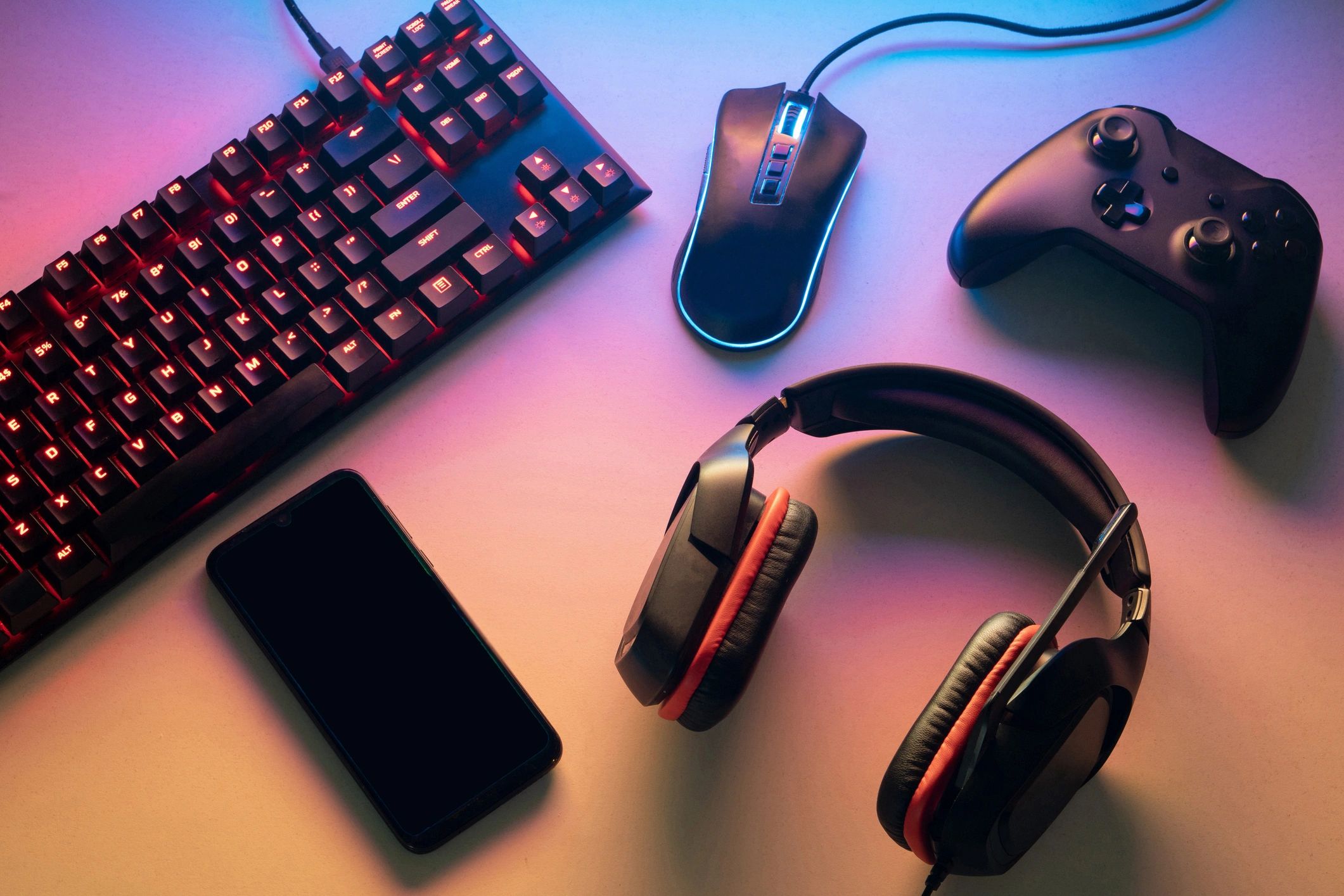 Gaming setup with keyboard, mouse, controller, headset, and smartphone on a colorful desk