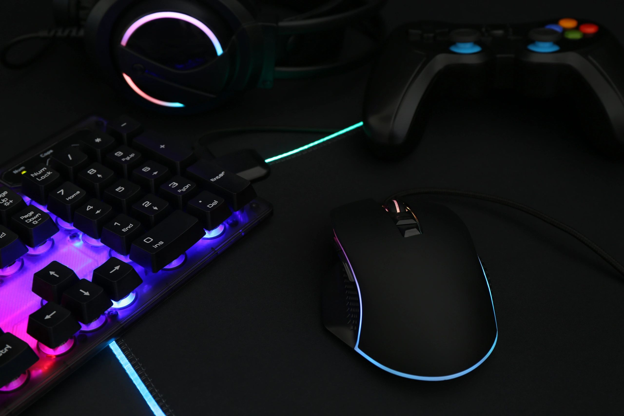 Computer mouse, RGB keyboard, headset and game controller on dark background, closeup